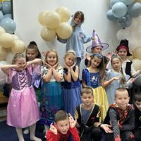 Dzieci przebrane w bajkowe stroje - górny rząd od lewej: kosmonauta, księżniczki, wróżki, pirat, król. Dolny rząd od lewej: spiderman, superbohater, batman. W tle balony żółte i niebieskie.