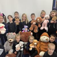 Grupa pierwszoklasistów ubranych na czarno trzyma w rękach maskotki. W większości są to pluszowe misie. 