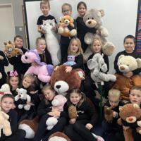 Grupa pierwszoklasistów ubranych na czarno trzyma w rękach maskotki. W większości są to pluszowe misie. 