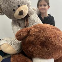 Dziewczynka w otoczeniu dwóch dużych pluszowych miśków - szarego i brązowego.