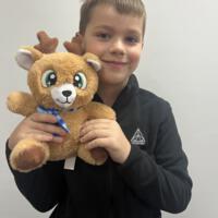 Chłopiec ubrany na czarno trzyma w ręku maskotkę - małego renifera.