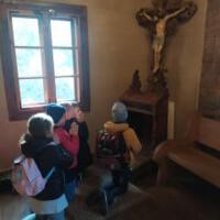 Na zdjęciu dzieci z wychowawcami wewnątrz kościoła/cerkwi. Niektóre dzieci klęczą przed krzyżem inne siedzą w ławce a jeszcze inne podziwiają ołtarz, malowidła, rzeźby.