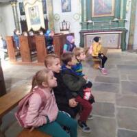 Na zdjęciu dzieci z wychowawcami wewnątrz kościoła/cerkwi. Niektóre dzieci klęczą przed krzyżem inne siedzą w ławce a jeszcze inne podziwiają ołtarz, malowidła, rzeźby.