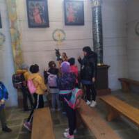 Na zdjęciu dzieci z wychowawcami wewnątrz kościoła/cerkwi. Niektóre dzieci klęczą przed krzyżem inne siedzą w ławce a jeszcze inne podziwiają ołtarz, malowidła, rzeźby.