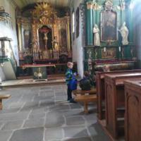 Na zdjęciu dzieci z wychowawcami wewnątrz kościoła/cerkwi. Niektóre dzieci klęczą przed krzyżem inne siedzą w ławce a jeszcze inne podziwiają ołtarz, malowidła, rzeźby.