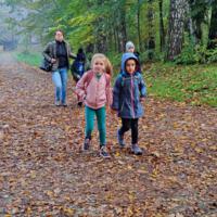 Na zdjęciach dzieci spacerują po skansenie. Trzymają się za ręce. W tle jesienna aura - drzewa z jeszcze zielonymi liśćmi na ziemi opadłe brązowe liście.
