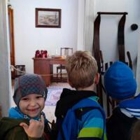 Dzieci znajdują się wewnątrz dawnej szkoły. Na ławkach uczniów są kartki do pisania i prawdziwe pióra. Pani wcieliła się w swoją rolę stając za biurkiem i uśmiechając się do dzieci. 