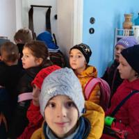 Dzieci znajdują się wewnątrz dawnej szkoły. Na ławkach uczniów są kartki do pisania i prawdziwe pióra. Pani wcieliła się w swoją rolę stając za biurkiem i uśmiechając się do dzieci. 