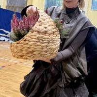 Na zdjęciu dyrektorka szkoły, trzymająca w ręku upominek - kosz wiklinowy z wrzosami.