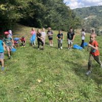 Na zdjęciach dzieci podczas spaceru po lesie, na polanie bawią się wspólnie przy użyciu chusty animacyjnej oraz bibuły w różnych kolorach. Jest słoneczna pogoda, na tle nieba pojawiają się białe chmury.