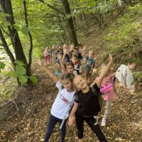 Na zdjęciach dzieci podczas spaceru po lesie, na polanie bawią się wspólnie przy użyciu chusty animacyjnej oraz bibuły w różnych kolorach. Jest słoneczna pogoda, na tle nieba pojawiają się białe chmury.