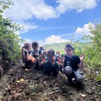 Na zdjęciach dzieci podczas spaceru po lesie, na polanie bawią się wspólnie przy użyciu chusty animacyjnej oraz bibuły w różnych kolorach. Jest słoneczna pogoda, na tle nieba pojawiają się białe chmury.