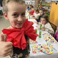 Dzieci przy wspólnym stole nakrytym białym obrusem jedzą tort urodzinowy.