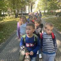 Dzieci spacerują po parku, jest słonecznie, na ziemi widać opadłe liście.