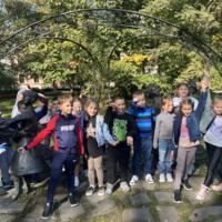 Dzieci spacerują po parku, jest słonecznie, na ziemi widać opadłe liście.