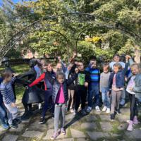 Dzieci spacerują po parku, jest słonecznie, na ziemi widać opadłe liście.