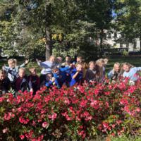 Dzieci spacerują po parku, jest słoneczna pogoda, na ziemi widać opadłe liście.