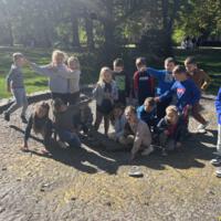 Dzieci spacerują po parku, jest słoneczna pogoda, na ziemi widać opadłe liście.