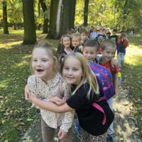 Dzieci spacerują po parku, jest słoneczna pogoda, na ziemi widać opadłe liście.