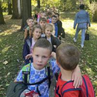 Dzieci spacerują po parku, jest słoneczna pogoda, na ziemi widać opadłe liście.