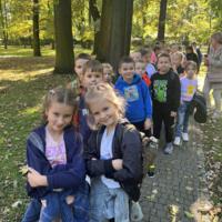 Dzieci spacerują po parku, jest słoneczna pogoda, na ziemi widać opadłe liście.