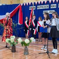 Pani dyrektor oraz wójt zabierają głos w uroczystości. W tle napis GMINNE ROZPOCZĘCIE ROKU SZKOLNEGO 2023-2024. Z boku stoją dwie dziewczynki ubrane galowo, które prowadziły część oficjalną akademii.