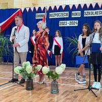 Pani dyrektor oraz wójt zabierają głos w uroczystości. W tle napis GMINNE ROZPOCZĘCIE ROKU SZKOLNEGO 2023-2024. Z boku stoją dwie dziewczynki ubrane galowo, które prowadziły część oficjalną akademii.