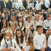 Na zdjęciach uczniowie szkoły, którzy oglądali akademię. Młodsze dzieci siedzą na ławeczkach. Starsze na krzesłach, najstarsi stoją z tyłu. Wszyscy są odświętnie ubrani.