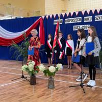 Pani dyrektor oraz wójt zabierają głos w uroczystości. W tle napis GMINNE ROZPOCZĘCIE ROKU SZKOLNEGO 2023-2024. Z boku stoją dwie dziewczynki ubrane galowo, które prowadziły część oficjalną akademii.