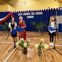 Pani dyrektor oraz wójt zabierają głos w uroczystości. W tle napis GMINNE ROZPOCZĘCIE ROKU SZKOLNEGO 2023-2024. Z boku stoją dwie dziewczynki ubrane galowo, które prowadziły część oficjalną akademii.