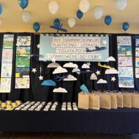 Na zdjęciu prezentacja prac oraz nagród dla uczestników konkursu. Na granatowym tle rozwieszona dekoracja w postaci chmur.