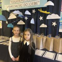 Dzieci oglądające prace. W tle na granatowej kotarze chmury oraz samoloty