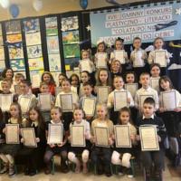 Grupa dzieci które brały udział w konkursie ubrane są galowo, każdy trzyma w ręku dyplom za udział w konkursie.