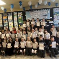 Grupa dzieci które brały udział w konkursie ubrane są galowo, każdy trzyma w ręku dyplom za udział w konkursie.