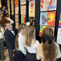 Dzieci oglądające prace. W tle na granatowej kotarze chmury oraz samoloty