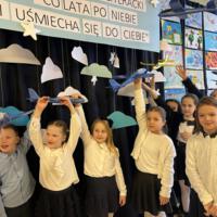 Dzieci oglądające prace. W tle na granatowej kotarze chmury oraz samoloty